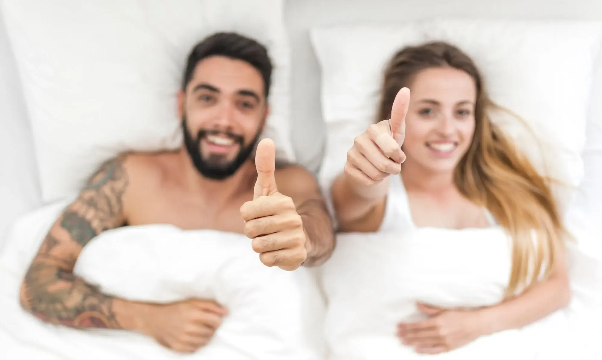 Mann und Frau in einem Bett halten beide den Daumen hoch