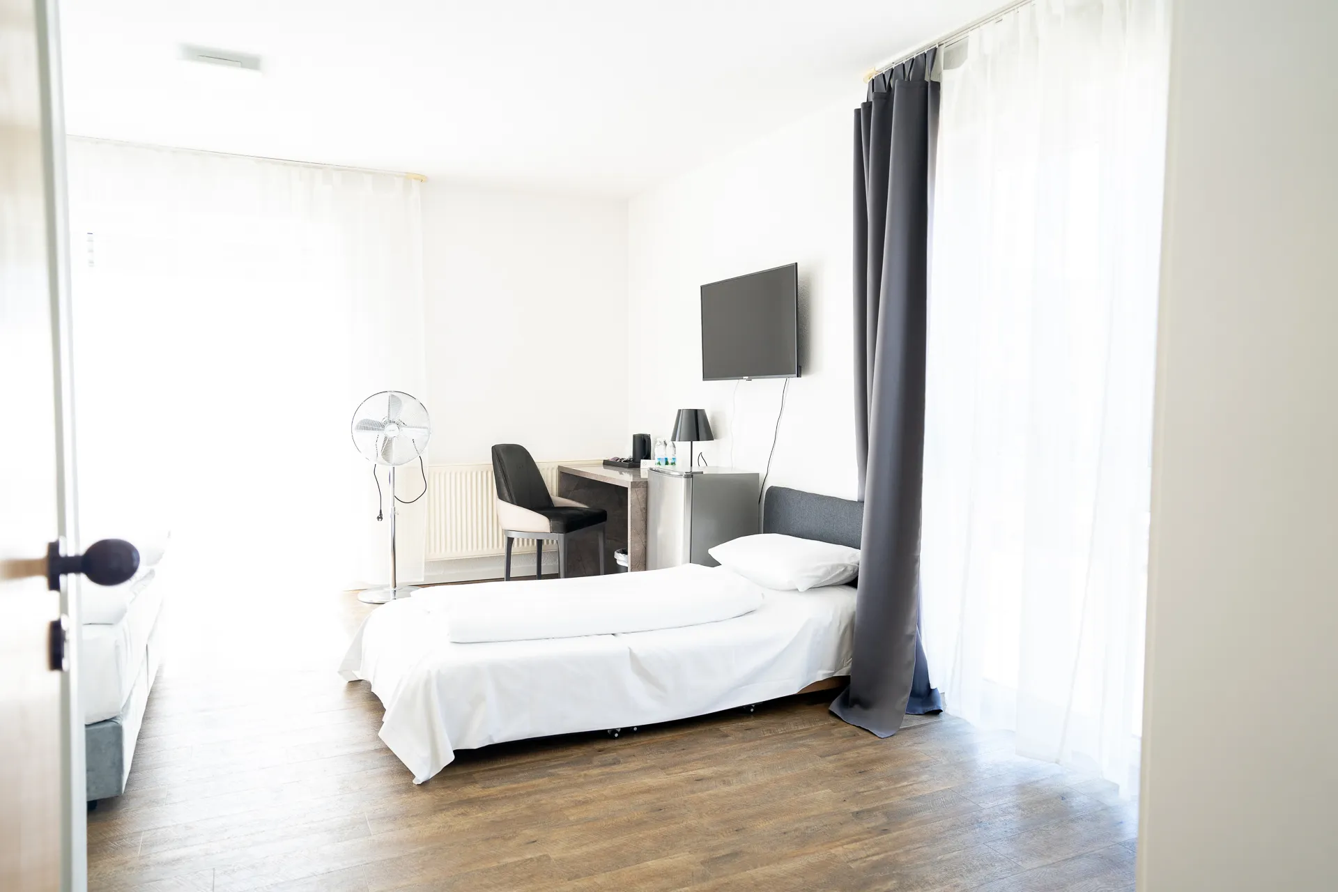 Hotelzimmer mit Drei Schlafmöglichkeiten, Wand-TV und minimalistischer Einrichtung.