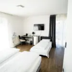 Hotelzimmer mit drei Betten, Schreibtisch und Fernseher